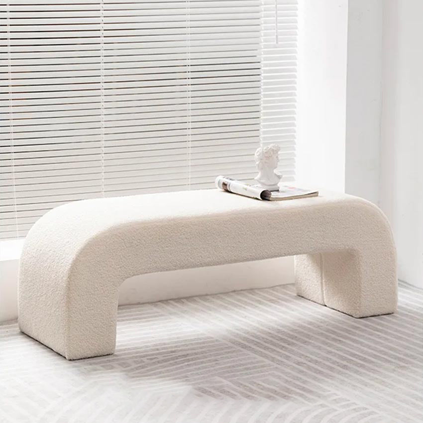 Banc en laine d’agneau blanc disposé devant un canapé gris dans un salon scandinave lumineux, ambiance cosy et raffinée.