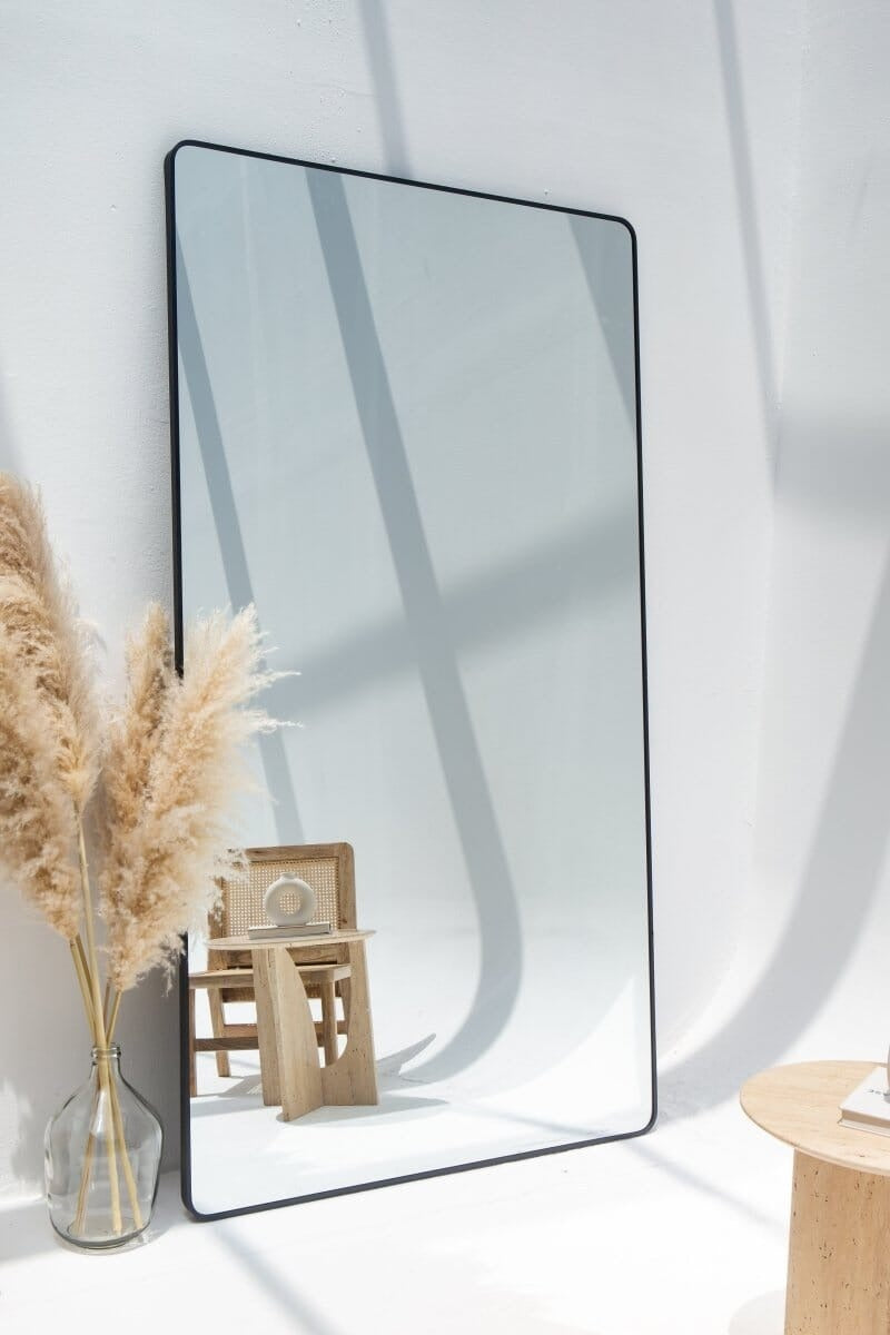 Miroir Adeline noir posé au sol – design épuré et reflet lumineux pour chambre moderne.